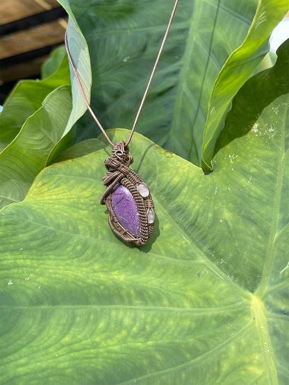 purpurite and rose quartz pendant close up shot on leaf with chain shown in the sun