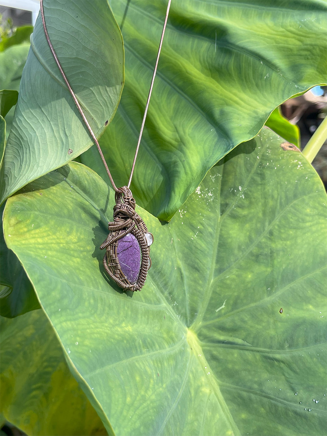 purpurite and rose quartz pendant close up shot on leaf with chain shown 